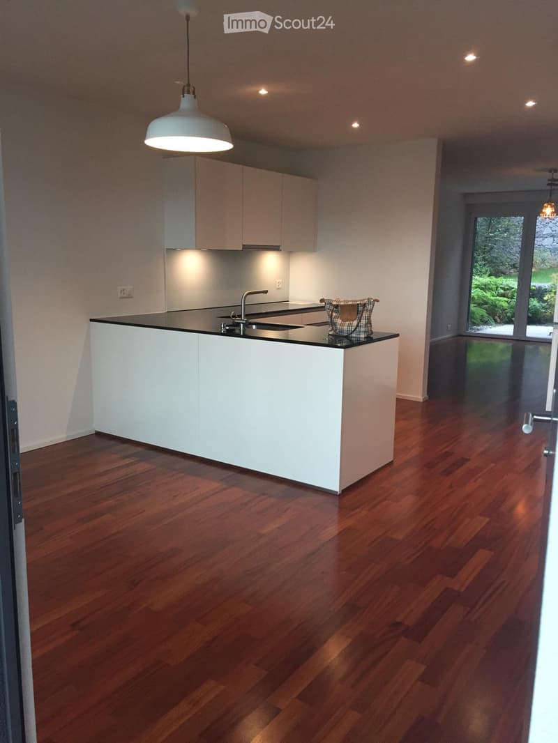 Modern kitchen with white cabinets, a central island, wooden flooring, and a pendant light fixture.