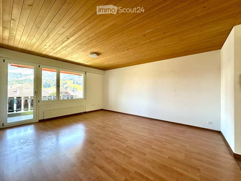 Empty room with wooden flooring, white walls, and large windows offering a view of the outdoors.