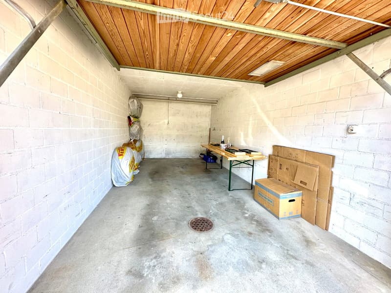 Empty garage with concrete floor, white brick walls, wooden ceiling, and some stacked boxes and bags along the walls.