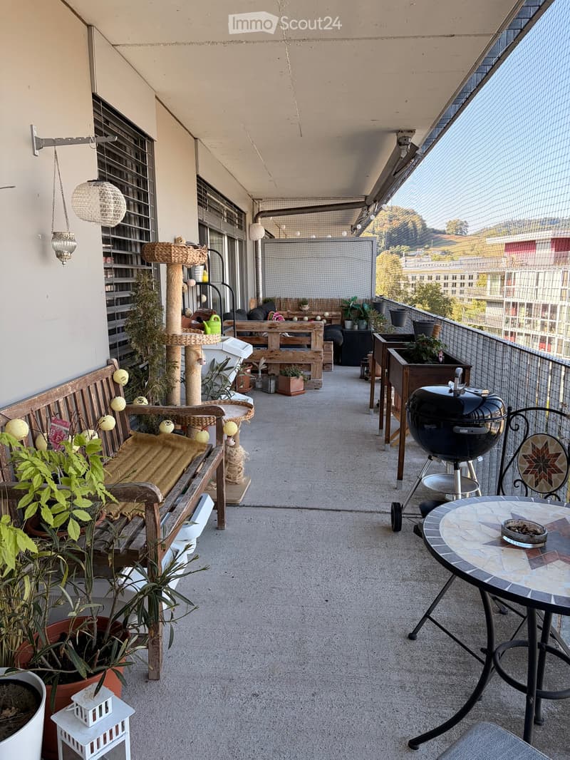Balcony with wooden bench, round table, chairs, cat tree, grill, and potted plants, overlooking a cityscape.