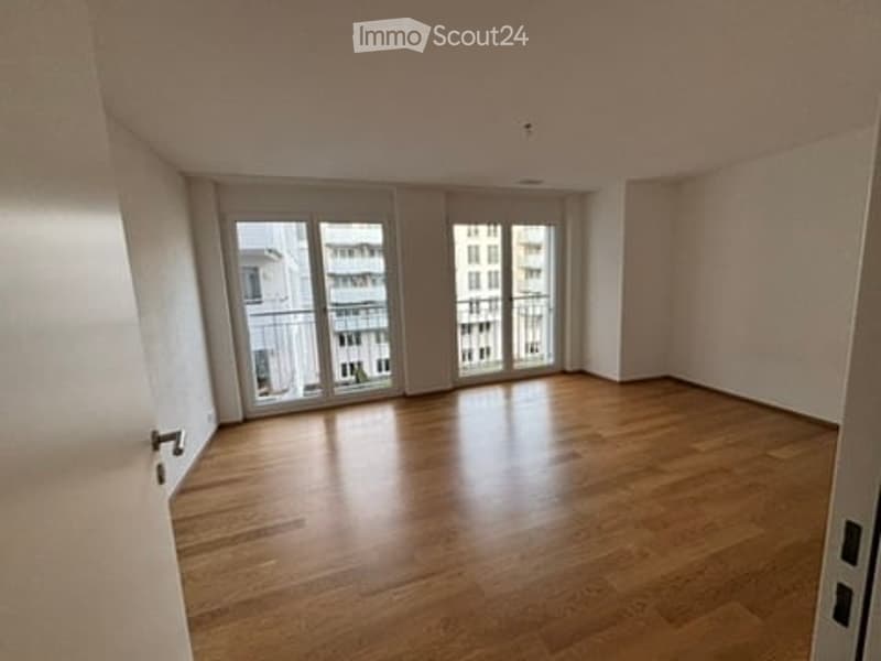 Empty room with wooden flooring, large windows, and a balcony access.