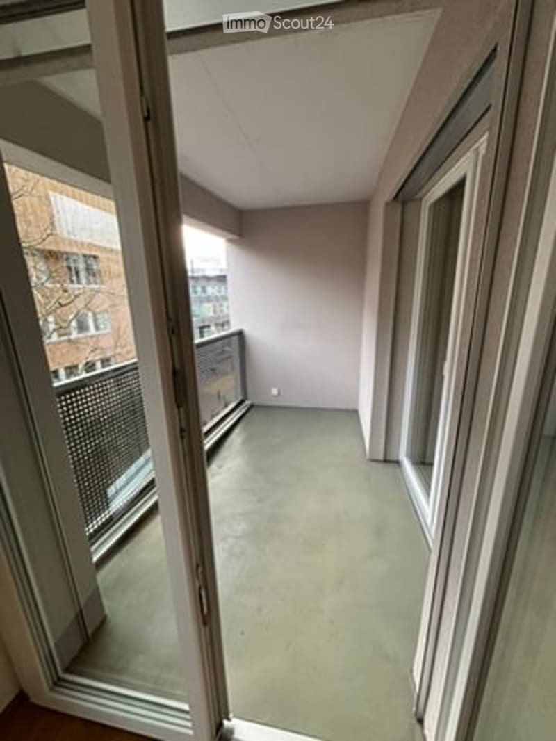 Empty balcony with grey walls, large windows, and a view of the city.