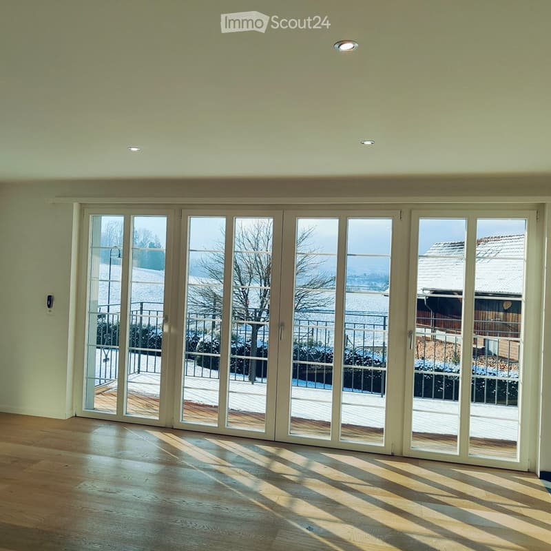 Empty room with light-colored walls, wooden flooring, and large sliding glass doors leading to a balcony or outdoor area.