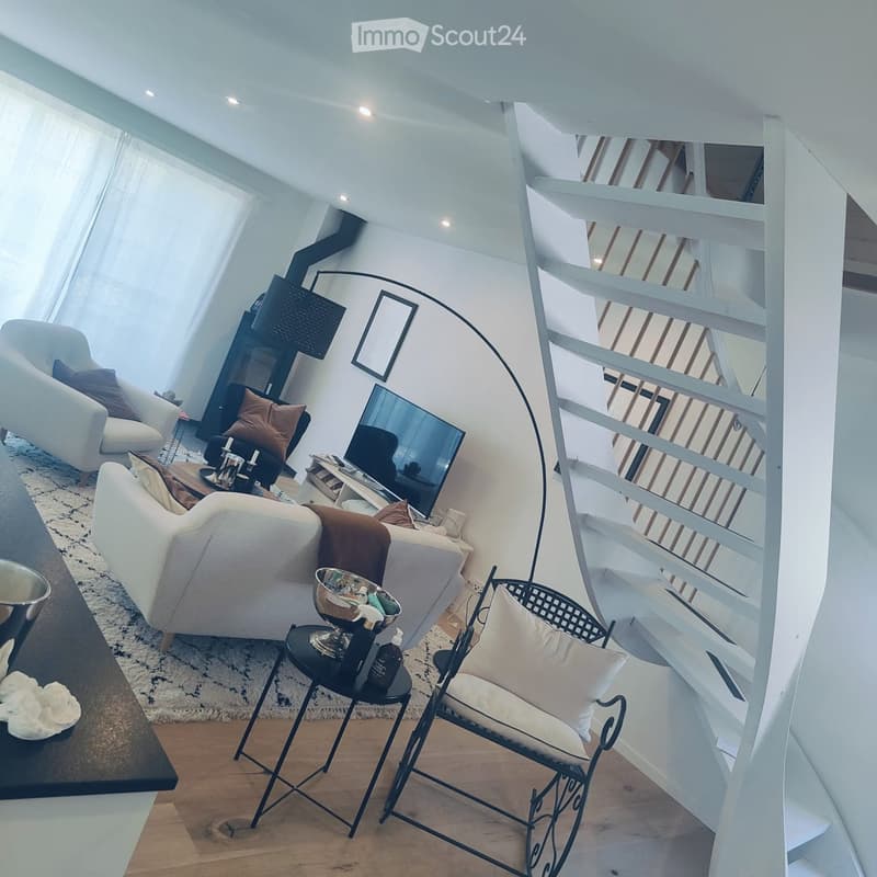 Modern living room with white walls, wooden floor, large windows, spiral staircase, sofa, chairs, coffee table, and decorative items.