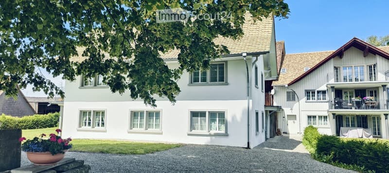 Two-story house with white exterior, multiple windows, tiled roof, and a covered balcony area with outdoor furniture.