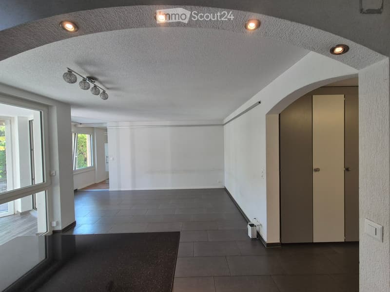 Empty hallway with dark tiled floor, white walls, recessed ceiling lights, and a door at the end.