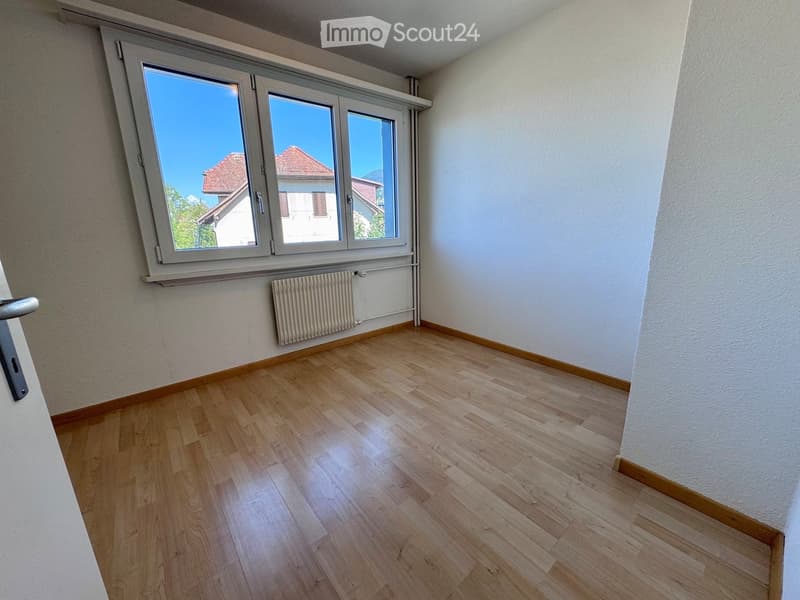 Empty room with wooden flooring, white walls, large windows, and a radiator. No furniture or equipment present.