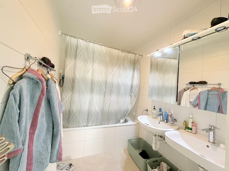 Modern bathroom with a bathtub, double sink, large mirror, and neatly arranged towels and toiletries.