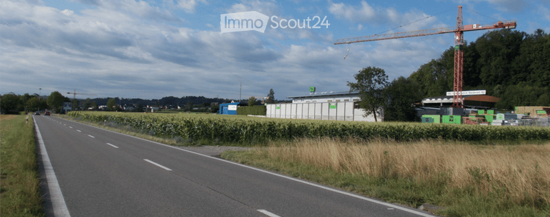Roadside view of a construction site with a large crane, temporary fencing, and a small building with signage.