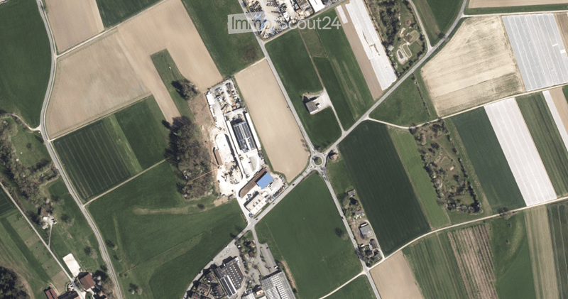 Aerial view of a large industrial building surrounded by agricultural fields and a parking area.