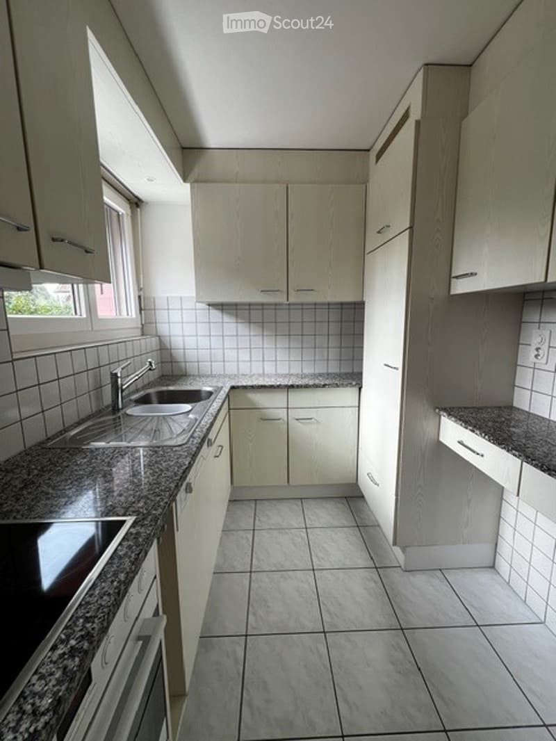 Modern kitchen with light wood cabinets, tiled walls, and a built-in washing machine. The space features a clean, minimalist design with ample storage and a central island.