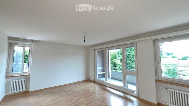 Empty room with wooden flooring, large windows, and a sliding glass door leading to a balcony.