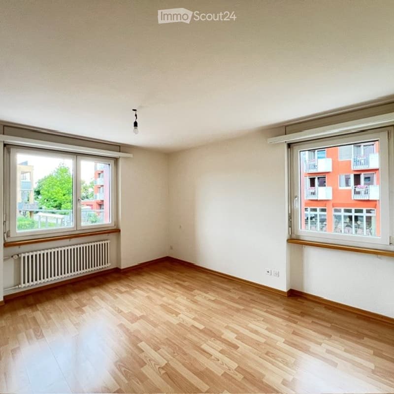 Empty room with wooden flooring, white walls, and large windows offering a view of the outside. No furniture or equipment is present.
