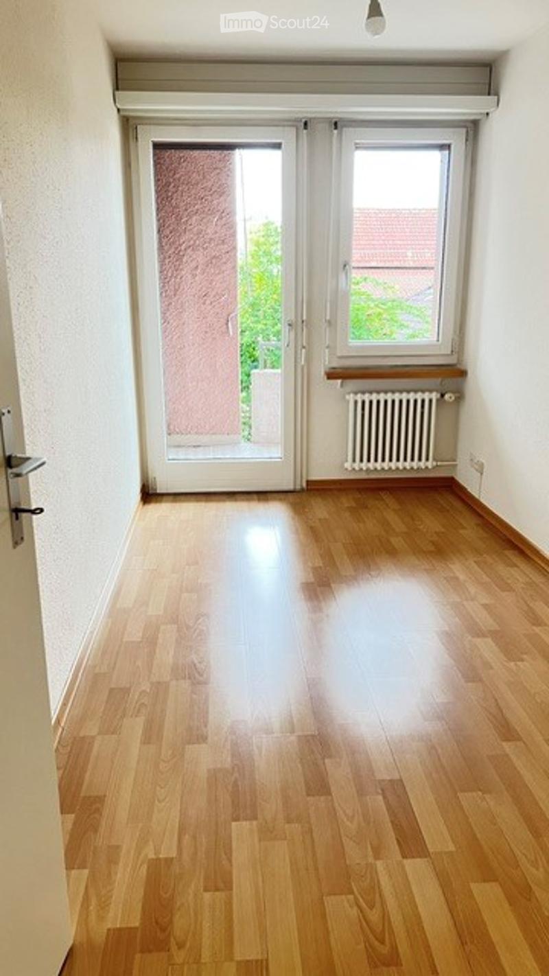 Empty room with wooden flooring, white walls, large window, and sliding glass door leading to a balcony.
