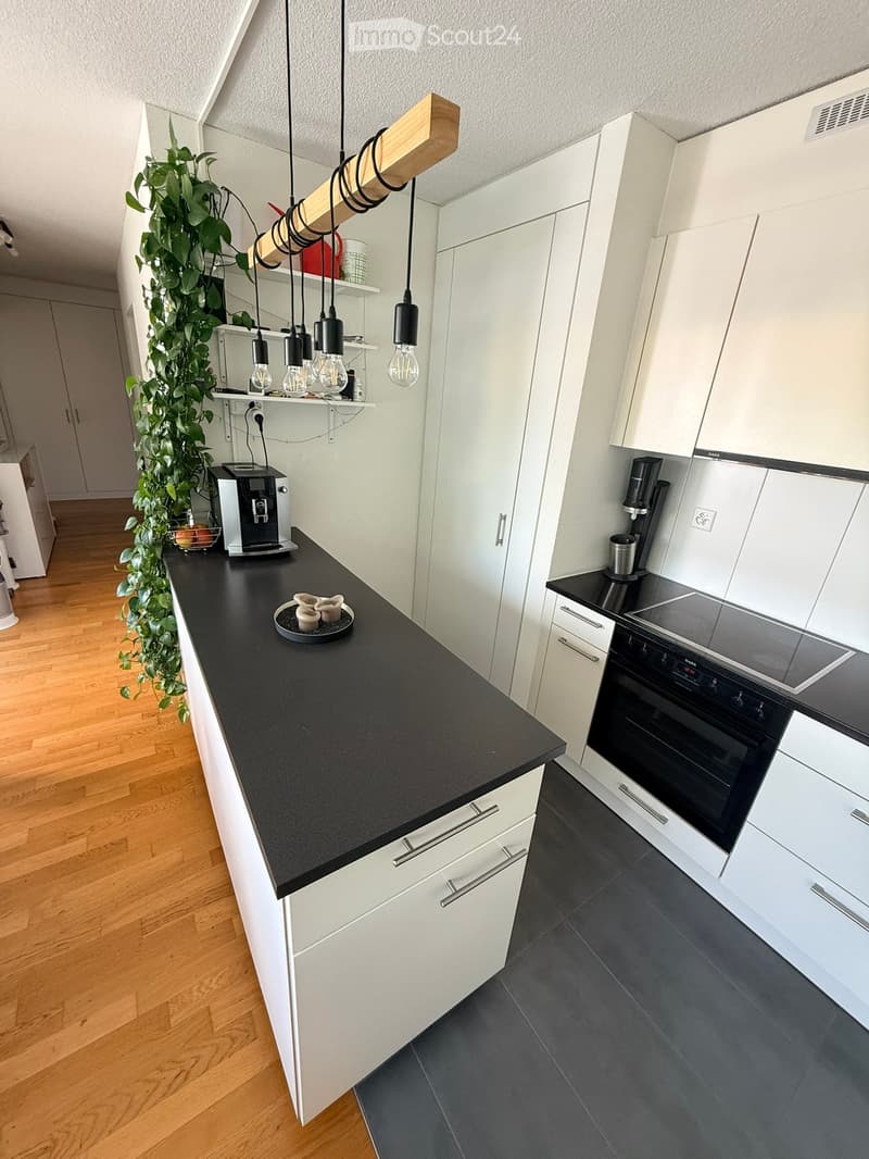 Modern kitchen with white cabinets, black countertops, and a pendant light fixture. Features a coffee maker, oven, and induction stove.