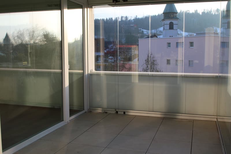 Modern balcony with large glass sliding doors, tiled floor, and scenic view of town and mountains.
