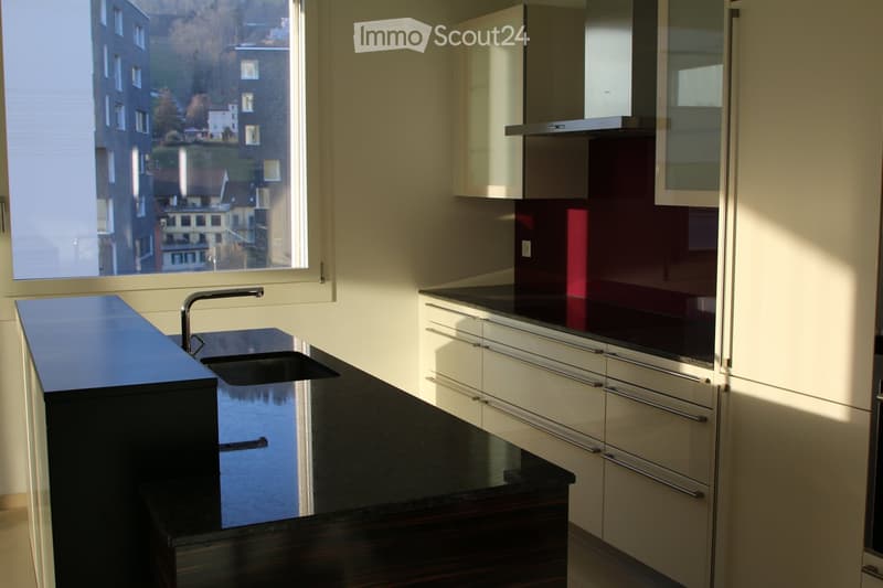 Modern kitchen with sleek black countertops, white cabinets, and a stainless steel sink and faucet. Large window offers a scenic view of the city and water.