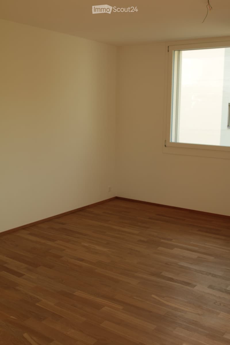 Empty room with wooden flooring and light-colored walls, featuring a large window on one side.