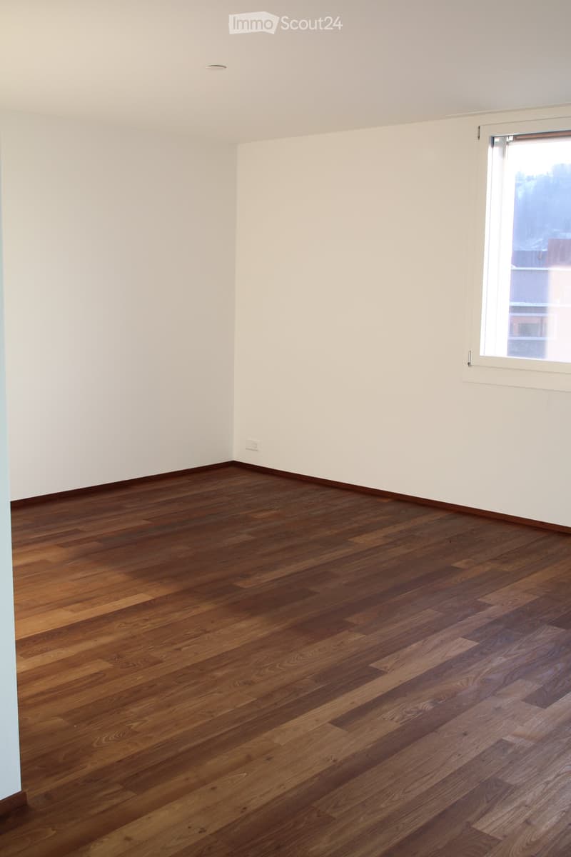Empty room with light-colored walls and dark wooden flooring, featuring a single window on one wall.