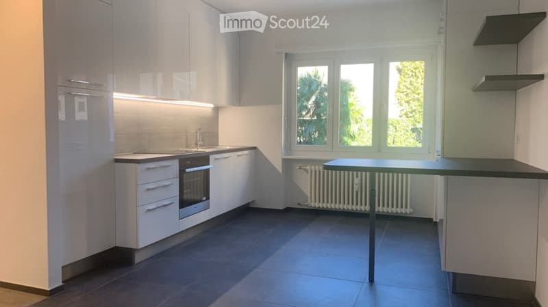 Modern kitchen with white cabinets, stainless steel appliances, dark countertops, and a small table with a metal frame.