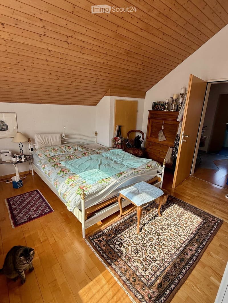 bedroom with bed, wooden floor, wooden ceiling, rug, lamp, cabinet, stool, cat
