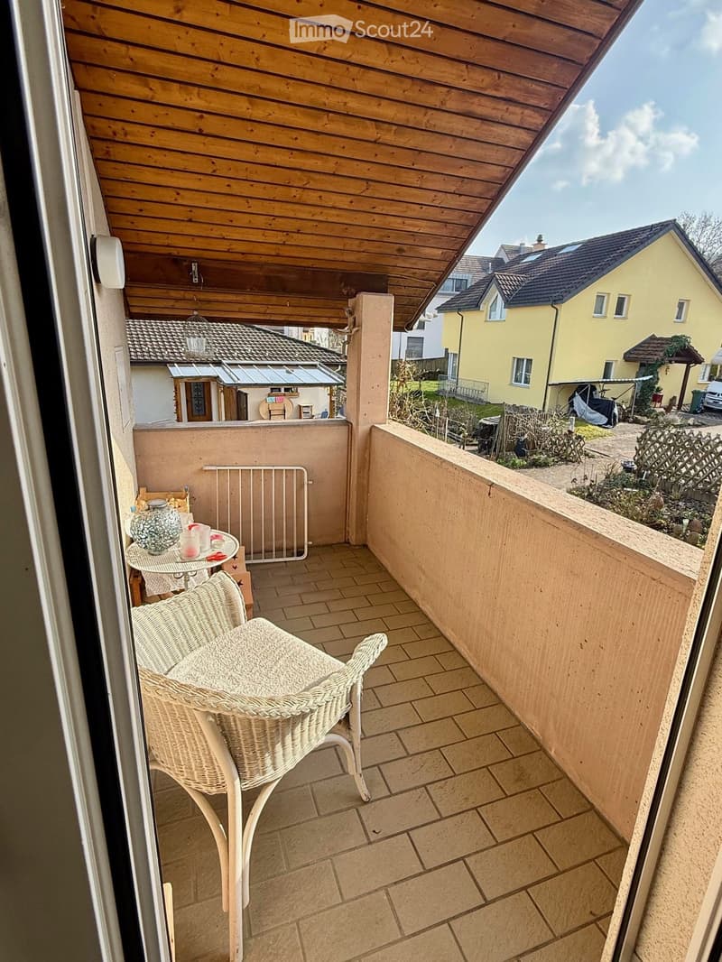 Balcony with wicker chair, tiled floor, small table, white railing, wooden ceiling