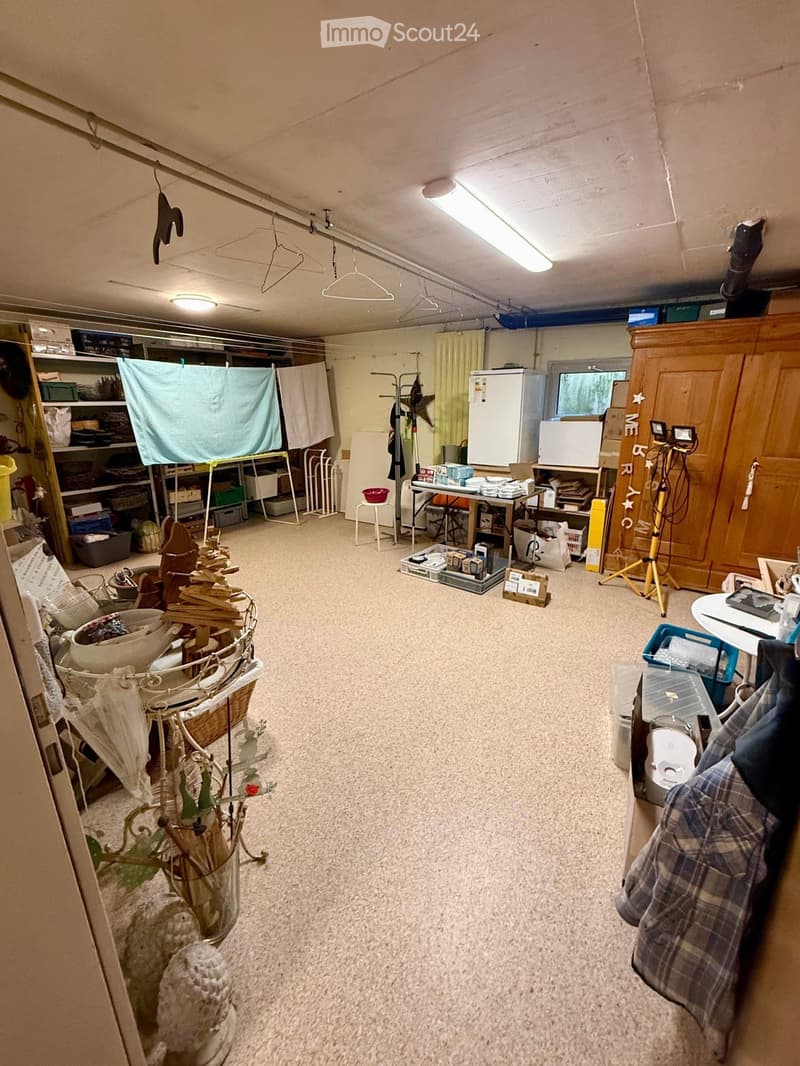 Storage room with various items, shelves, a table, a chair, a refrigerator, and a tripod.
