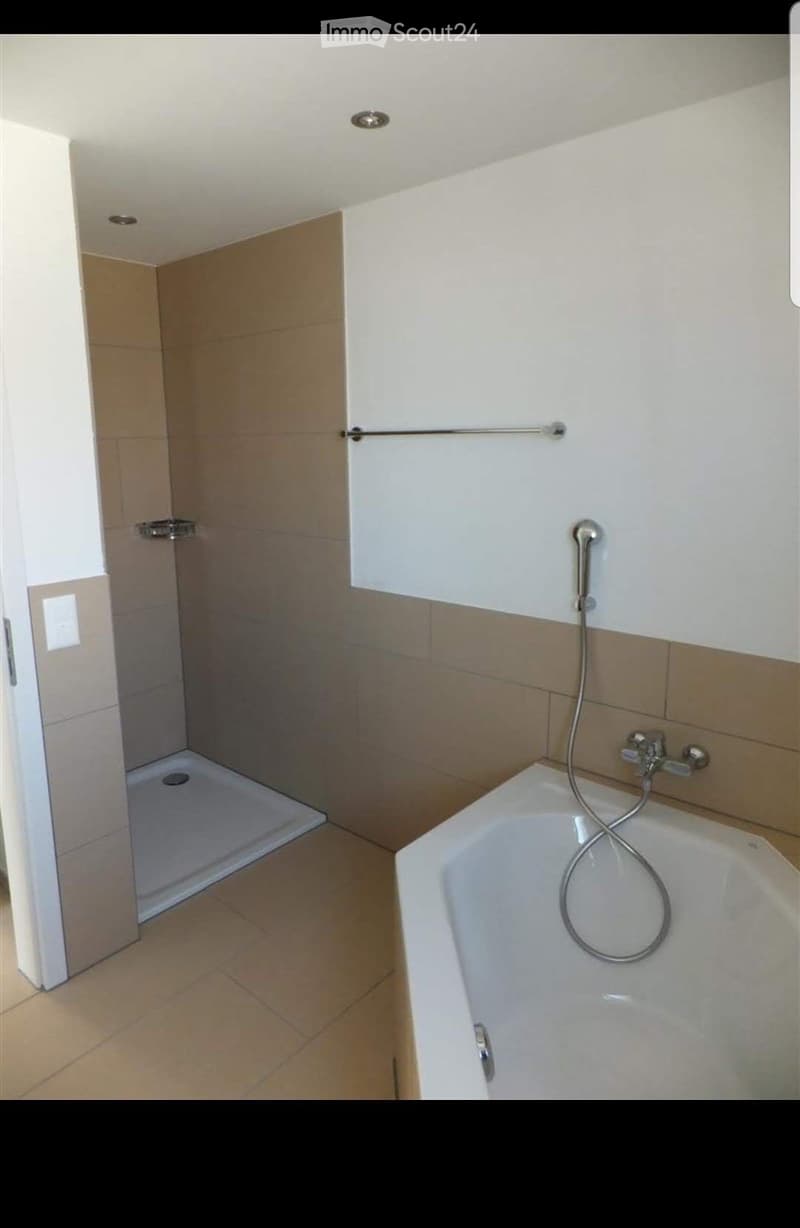 Modern bathroom with a bathtub, handheld shower, and a separate shower area with a glass enclosure. Light-colored tiles and a sleek design.