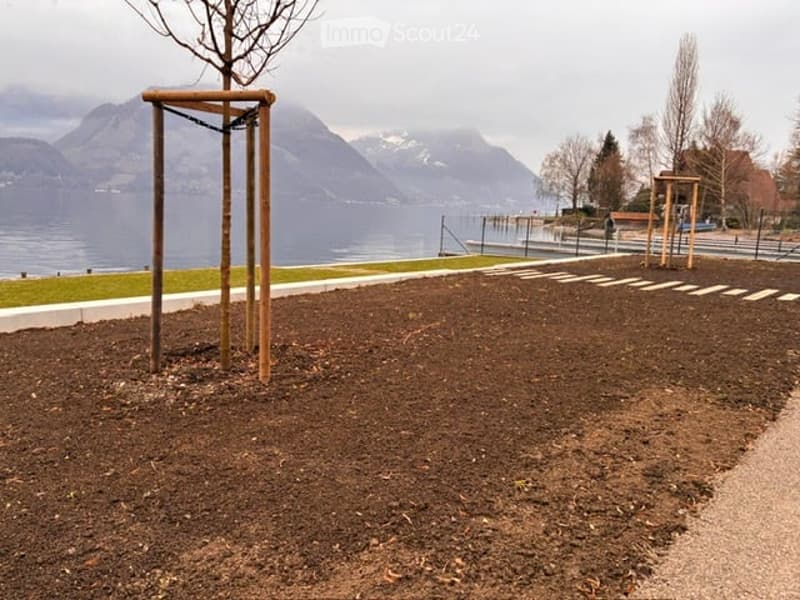 Outdoor park area with playground equipment, dirt ground, and scenic mountain and lake view in the background.