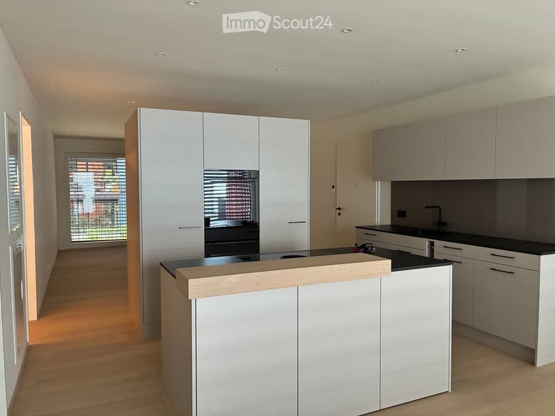 Modern kitchen with white cabinets, black countertops, and a central island. Features include a sink, faucet, and built-in appliances.