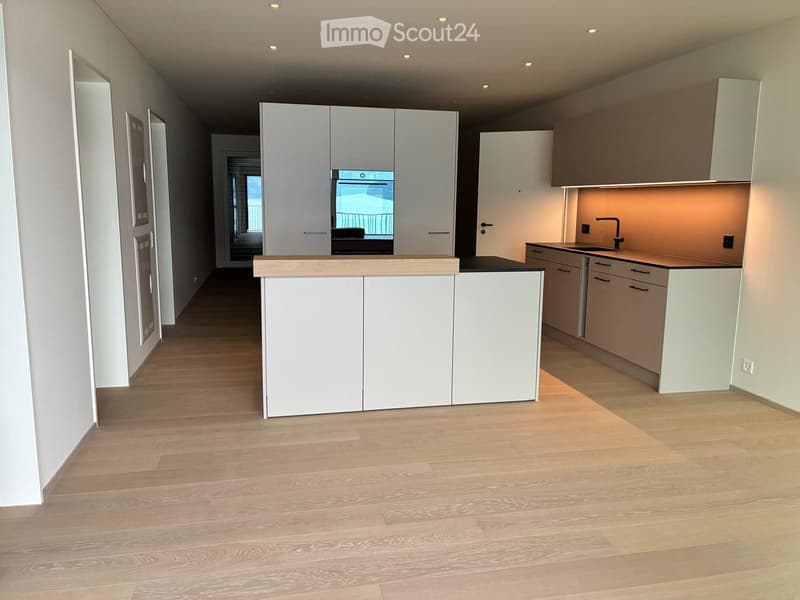 Modern kitchen with white cabinets, wooden countertops, and a central island. The floor is made of light wooden planks, and the space is well-lit with recessed lighting.