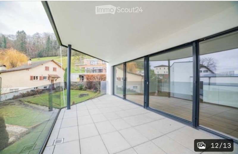 Modern balcony with large glass panels, tiled floor, and scenic view of surrounding houses and greenery.