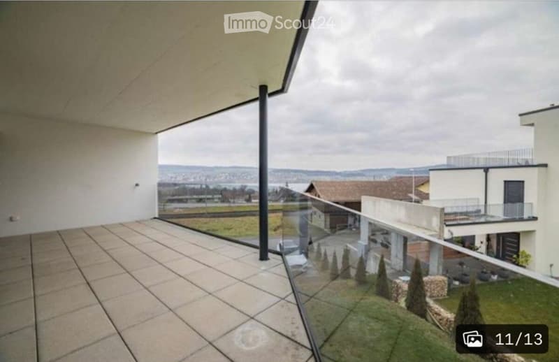 Modern balcony with tiled floor, glass railing, and scenic view of surrounding landscape and buildings.