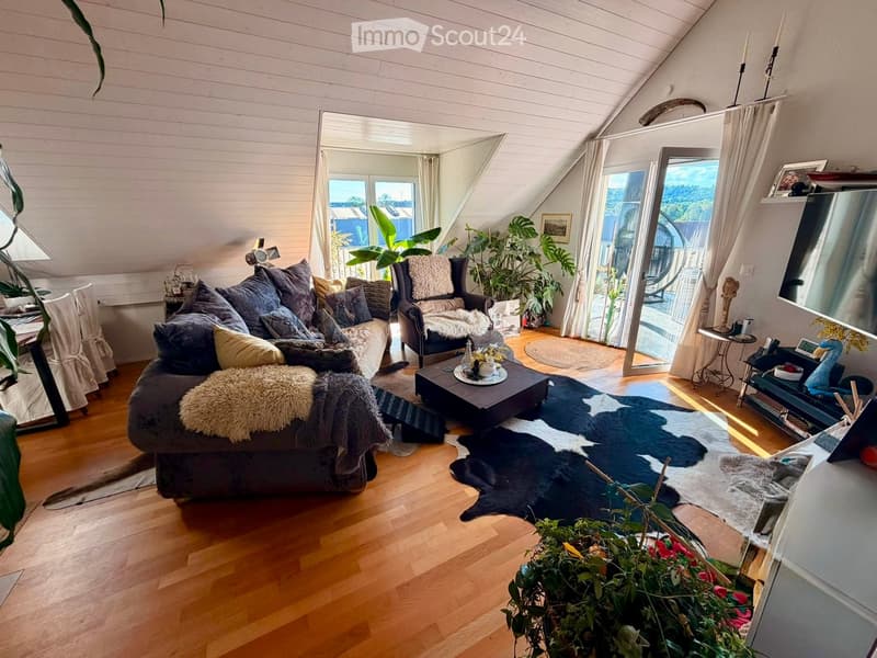 Living room with wooden flooring, slanted ceiling, large windows, sofa, coffee table, armchair, and decorative items.