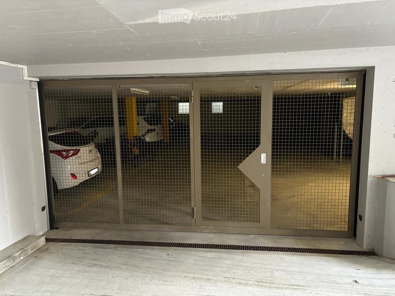 Underground parking area with a security gate, showing a white car and a motorcycle inside.