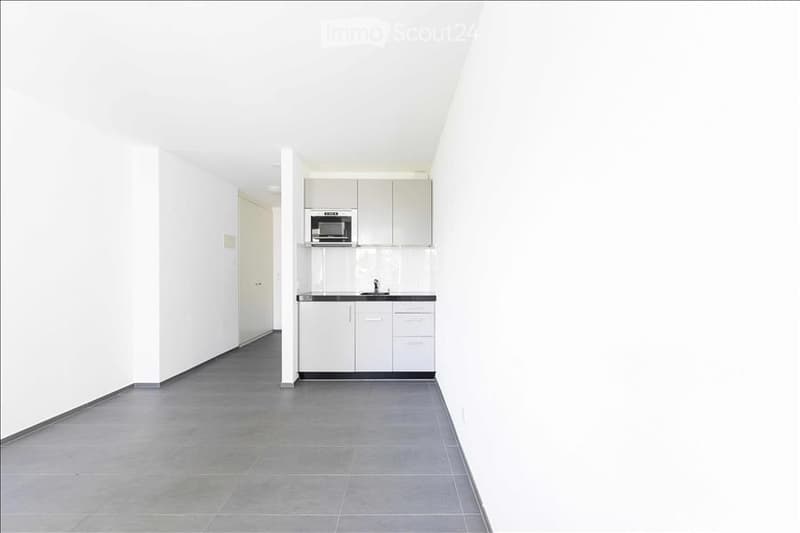 Empty kitchen with white cabinets, stainless steel microwave, and grey tiled floor.