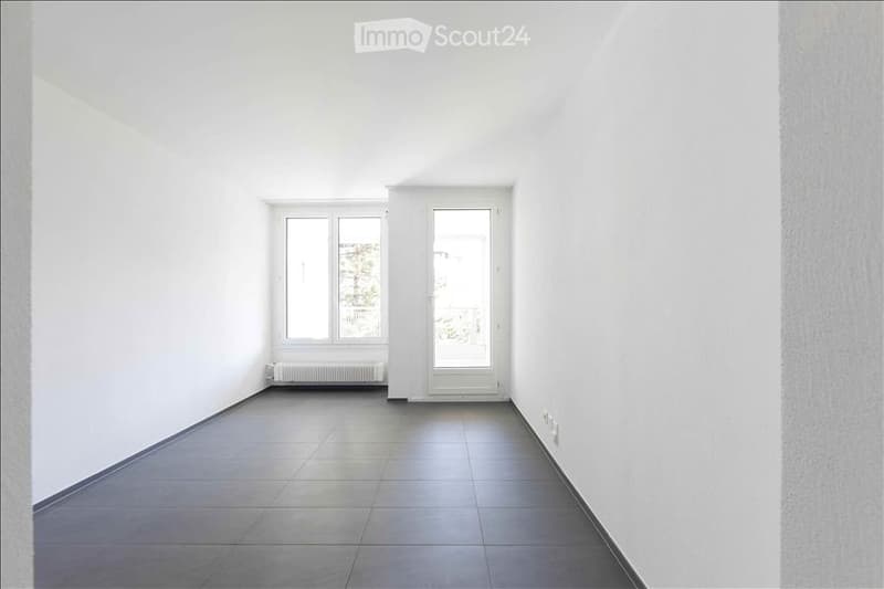 Completely empty room with white walls, tiled floor, and large windows. No furniture or equipment.