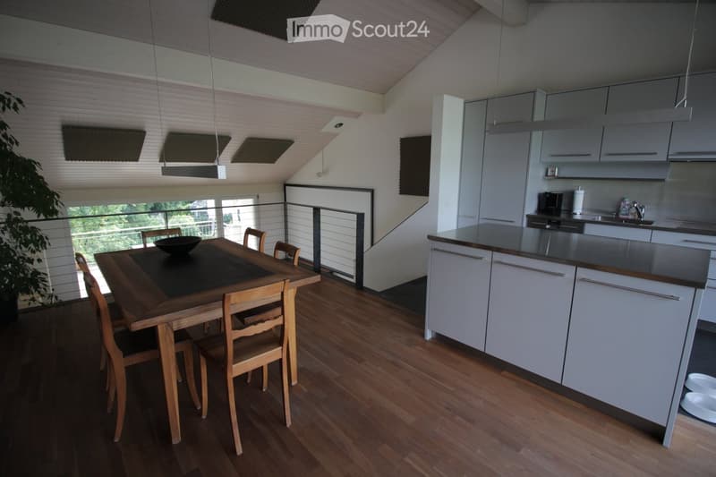 Open-plan kitchen and dining area with white cabinets, wooden dining table, chairs, and a view through a glass railing.