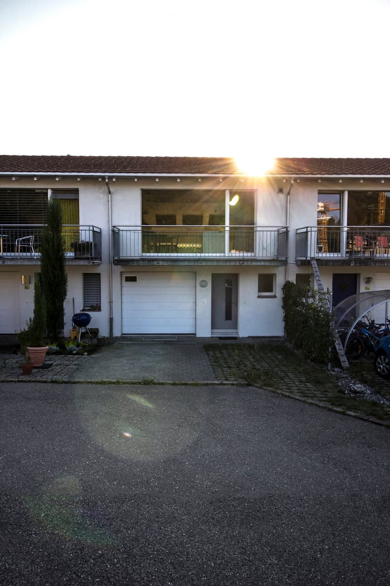 Two-story house with white exterior, multiple windows, balconies, garage, and small garden area.