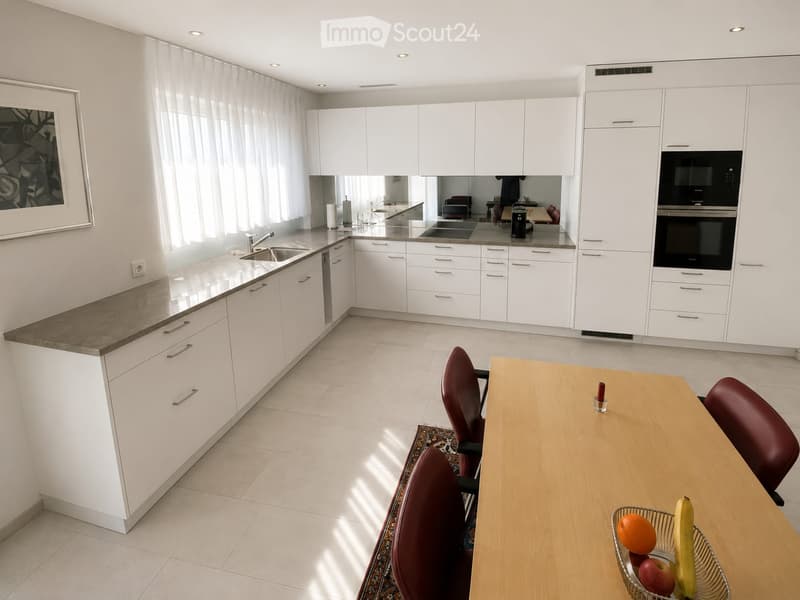 Modern kitchen with white cabinets, granite countertops, and stainless steel appliances. Includes a dining area with a wooden table and red chairs.