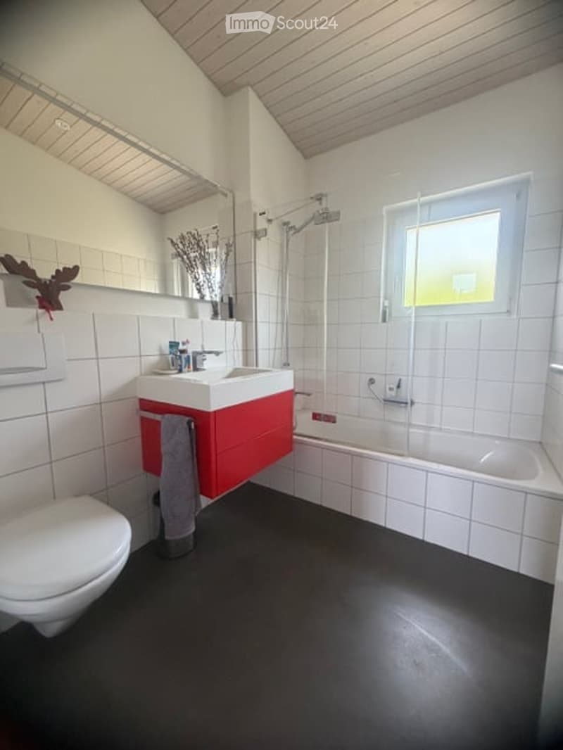 Modern bathroom with white tiles, black floor, red vanity cabinet, sink, bathtub, toilet, and a window providing natural light.
