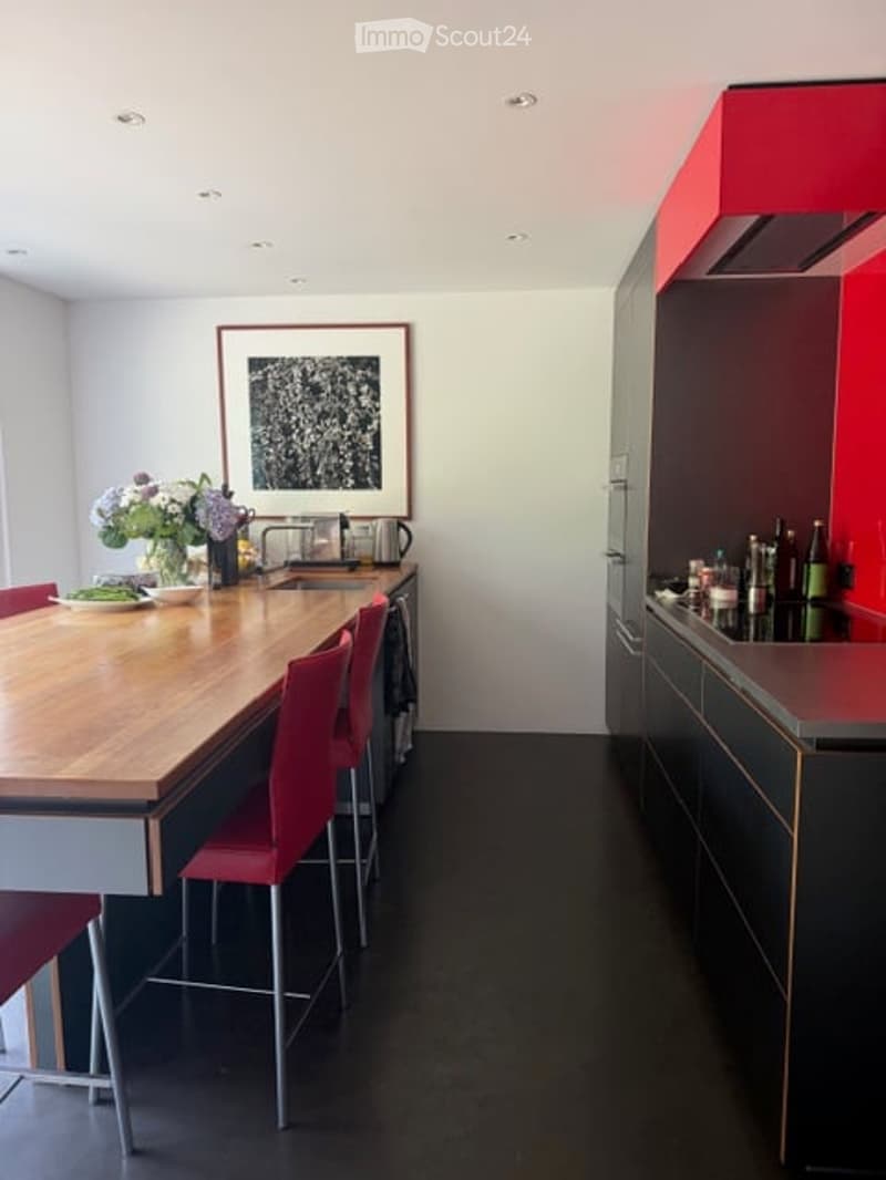 Modern kitchen with a wooden island, red bar stools, sleek black cabinets, and a stainless steel sink.
