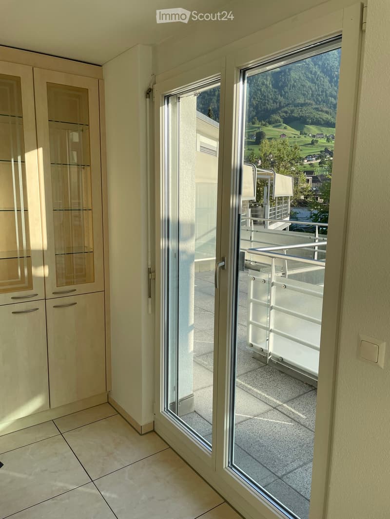 View of a balcony area with a glass door leading from an interior space, showing a scenic outdoor view of green hills and trees.