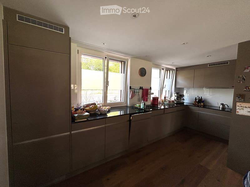 Modern kitchen with grey cabinets, black countertops, and stainless steel appliances. Features include a refrigerator, sink, coffee maker, and various kitchen items on the counter.