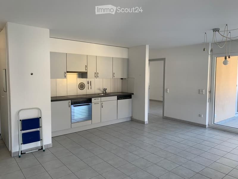 Empty kitchen and living area with white cabinets, stainless steel appliances, tiled floor, and a sliding glass door leading outside.