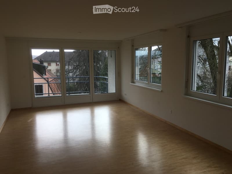 Empty room with wooden flooring, large windows, and a sliding door leading to a balcony.