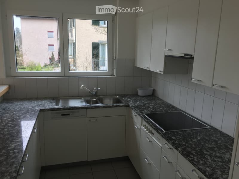 Modern kitchen with granite countertops, stainless steel sink, dishwasher, microwave, and stove. White cabinets and tiled backsplash.