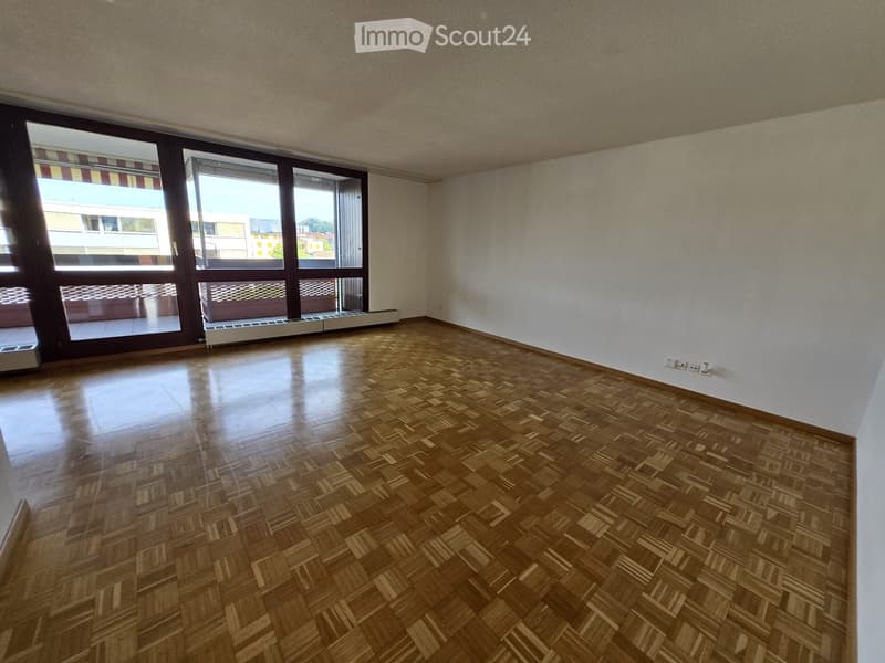 Empty room with wooden parquet flooring, white walls, large windows with blinds, and a radiator under the windows.