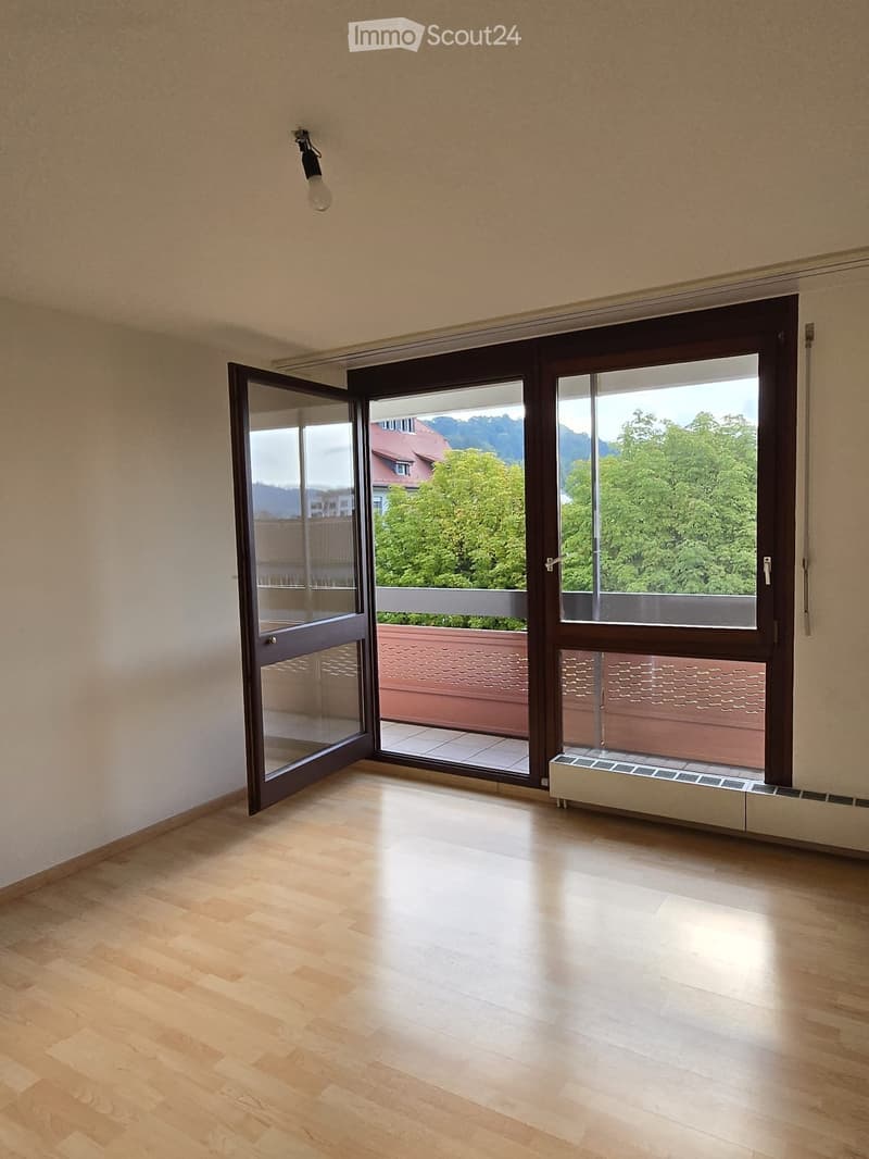 Empty room with wooden flooring, large sliding glass doors opening to a balcony, and a radiator below the window.