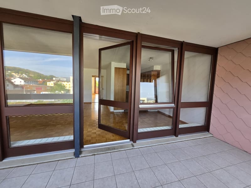Balcony with large sliding glass doors leading to an interior space, tiled floor, and a view of a town and hills.